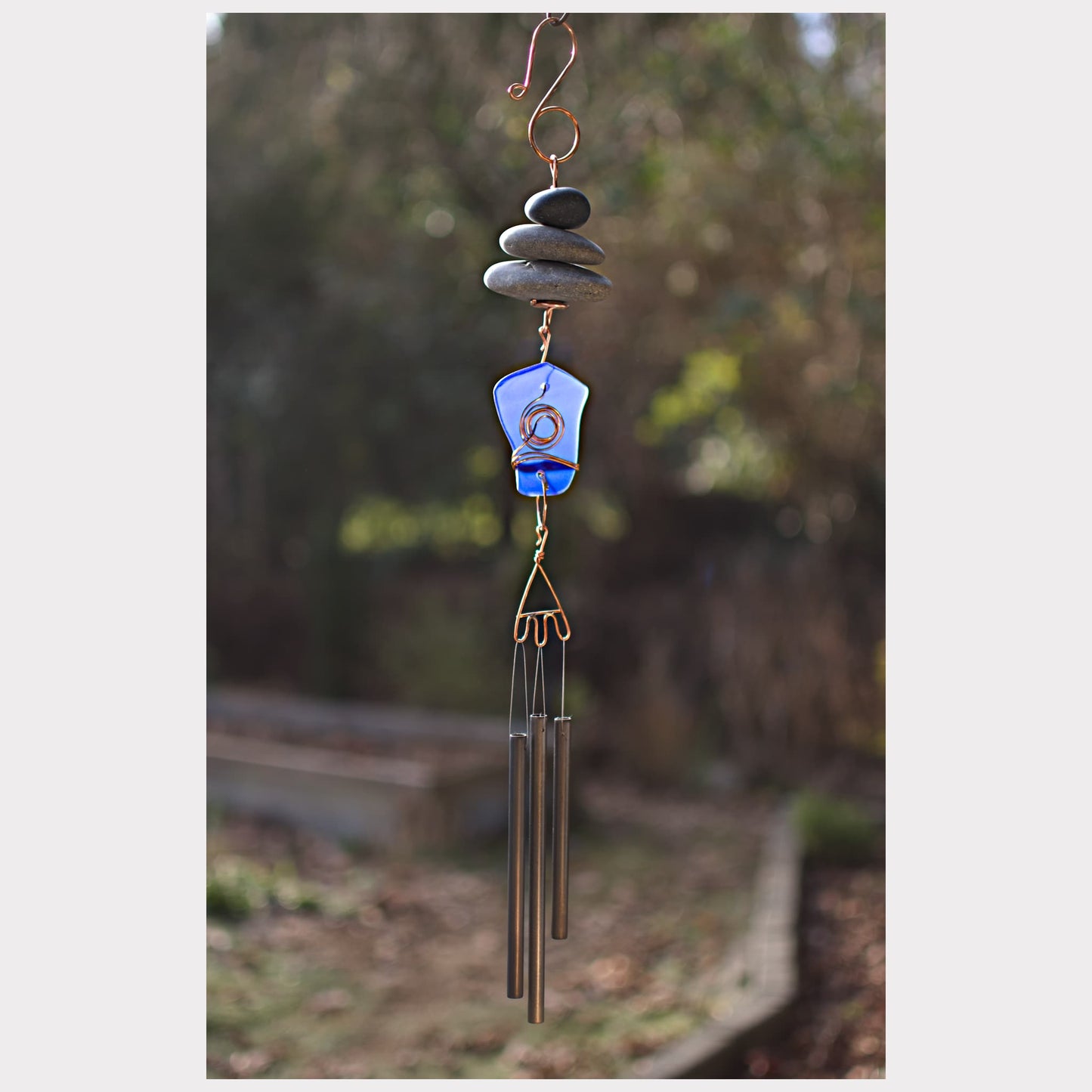Decorative wind chime with stones and a blue glass piece against a natural background
