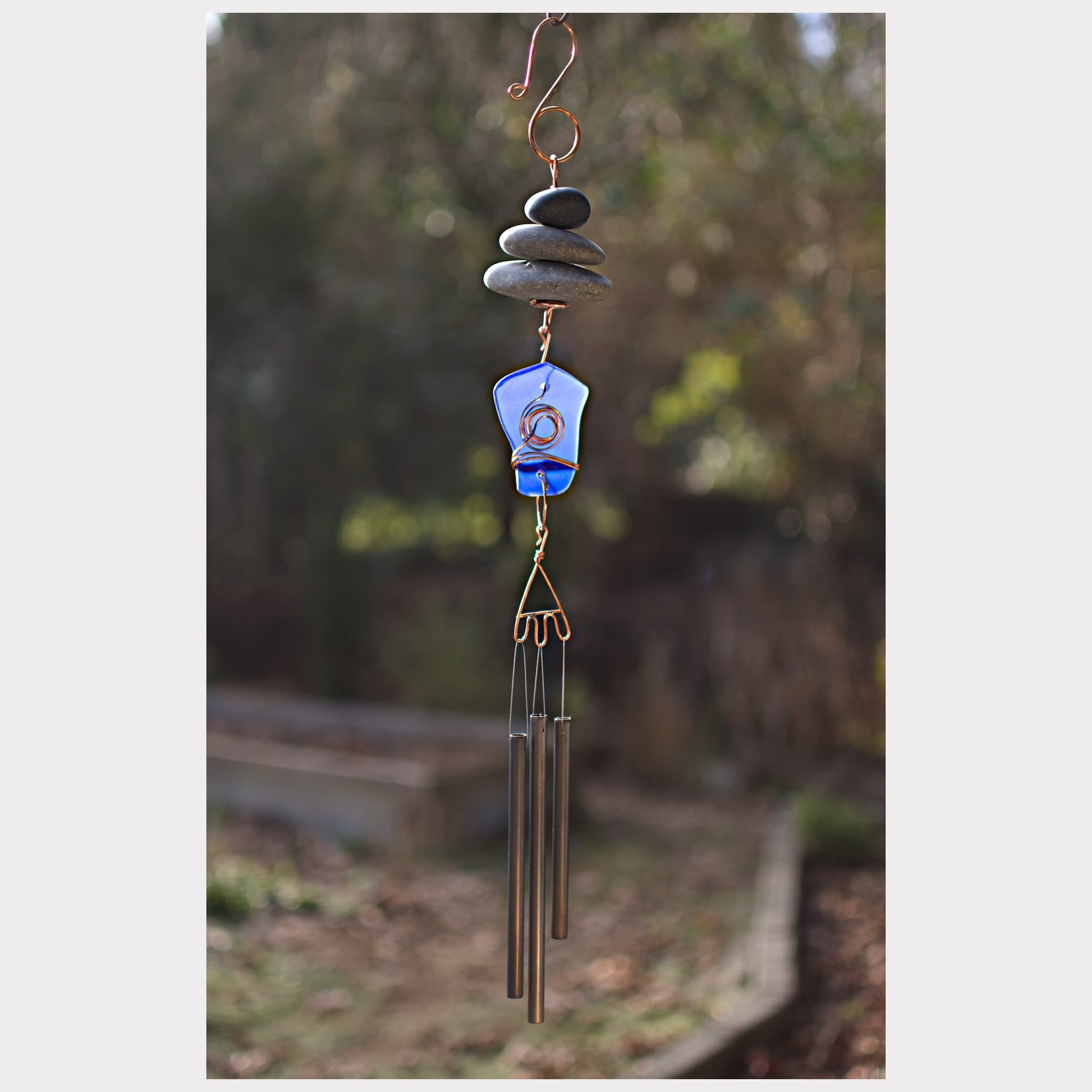 Decorative wind chime with stones and a blue glass piece against a natural background