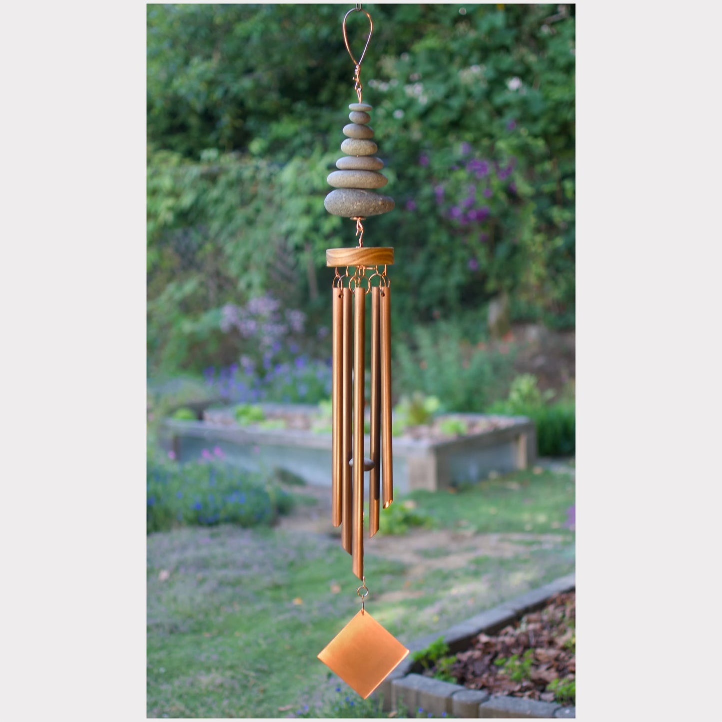Decorative wind chime with stones and metal tubes in a garden setting