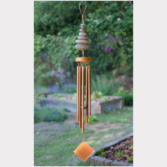 Decorative wind chime with stones and metal tubes in a garden setting