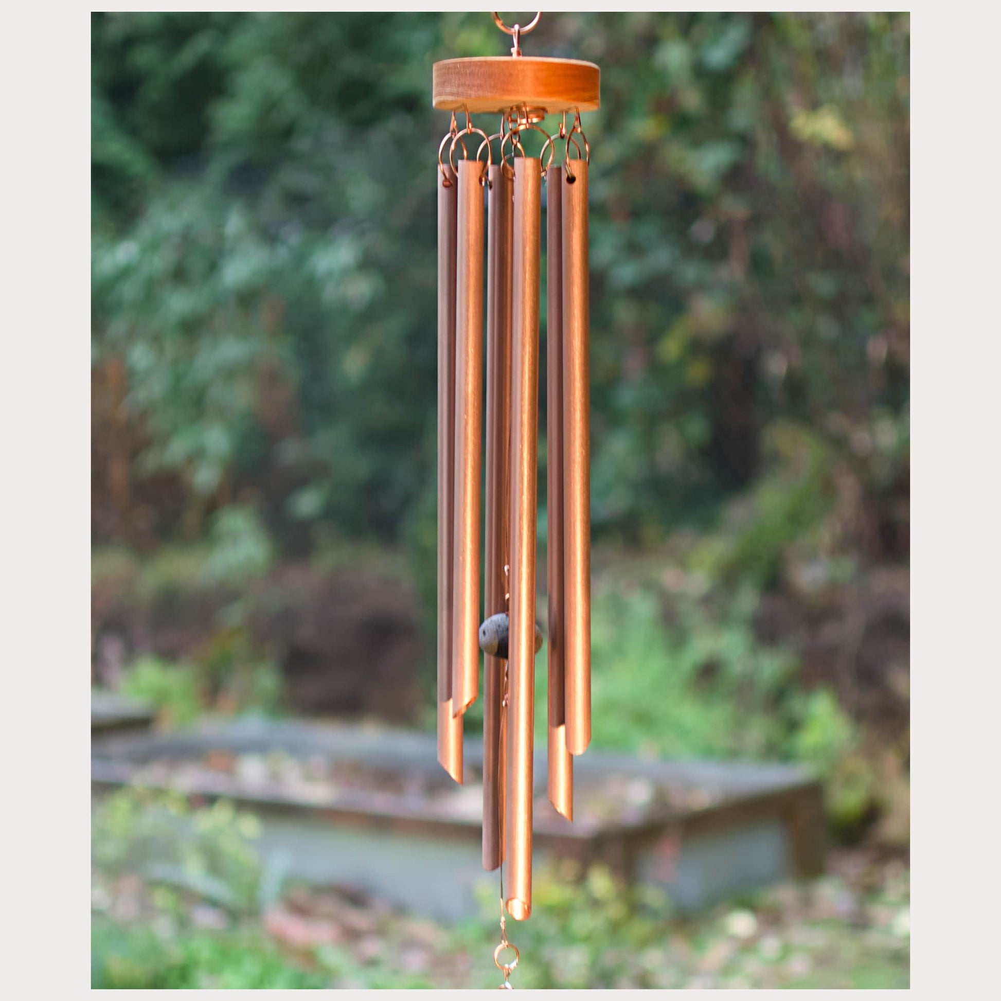 Copper wind chime with wooden top against a blurred garden background
