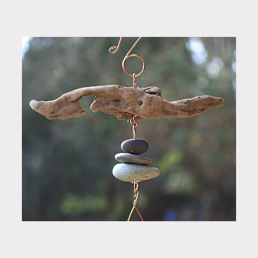 Driftwood and stone wind chime with a blurred natural background