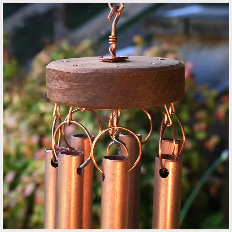 Copper wind chime with wooden top against a blurred natural background